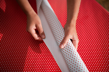 Hands wrapping a gift with red and white polka dot paper, focusing on the holiday spirit and...