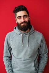 Fototapeta premium Casual Portrait of a Bearded Man in Grey Hoodie Against Red Background