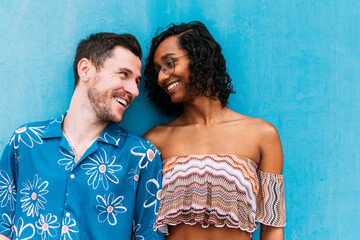 Young interracial couple smiling and embracing diversity against blue wall. Transgender woman