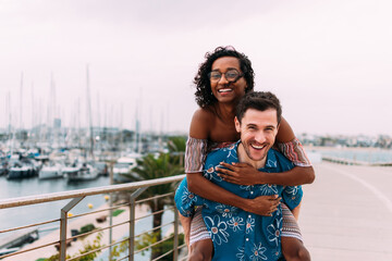 Young interracial couple piggybacking and having fun at the marina. Transgender woman