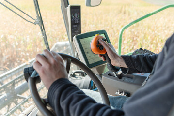 Farmer Operating Auger Joystick in Combine Harvesting Soybeans, Steering Wheel and Tractor Computer Visible in Field, Close-Up of Hand Controlling Farm Equipment During Busy Harvest Season