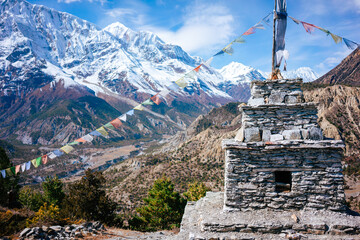 A stone chorten stands tall along the Annapurna Circuit, adorned with colorful prayer flags...