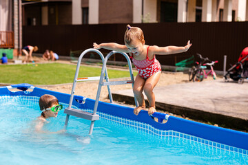 Happy little girl in red swimsuit jumping into outdoor swimming pool at home. Baby girl learning to swim. Water fun for children.
