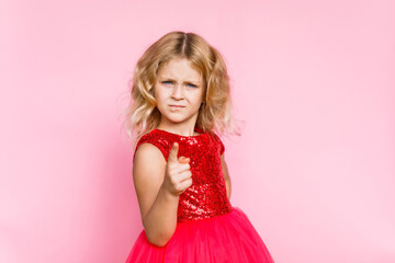 Girl with long hair in festive paper hat and dressy dress on pink background tossing gold confetti