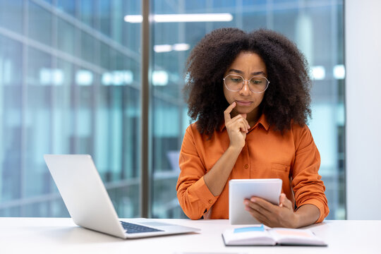 Thoughtful woman at work using a tablet and laptop in a modern office setting