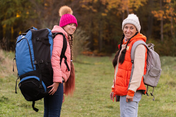 family walking in autumn forest with backpacks, girl in pink jacket, mother in orange sleeveless jacket, family in hat with pompoms, gen z