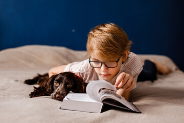 Little boy in glasses reading a storybook with his dog beside him