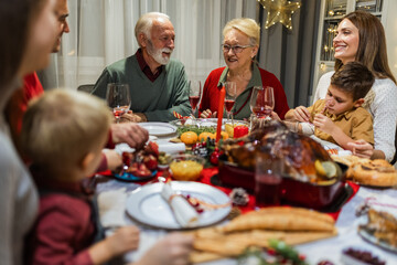Happy family having Christmas dinner with their grandparents. Eating homemade food, drinking beverages. Home is decorated for New Year's Eve and Christmas