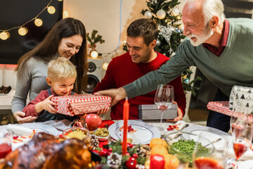 Grandparents giving presents to their grandchildren on Christmas Eve. Family having dinner.