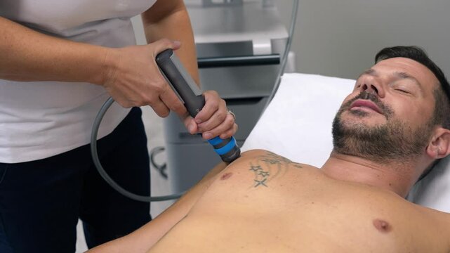 Expert administers targeted shockwave therapy to treat shoulder pain in a man