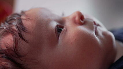 Close-up of a baby lying down, gazing upwards with curiosity and calmness. infant has a soft...