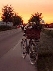 Fototapeta premium Una bicicleta antigua con una cesta llena de flores en una carretera solitaria durante la puesta de sol 