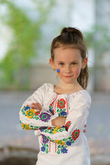 Little cute girl in Ukrainian traditional embroidered shirt and with Ukrainian flag on her cheek....