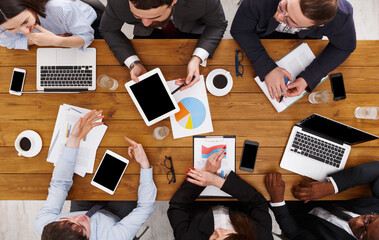 Business meeting top view. Busy people work in office, above view of wooden table with mobile phones, laptop, tablet and documents papers with diagram.