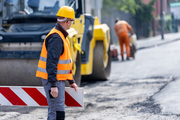 Construction worker directing traffic with safety barriers on a busy street under repair during the...