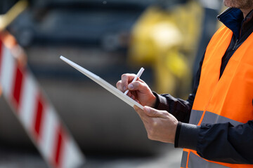 Construction worker taking notes while monitoring site activities at a busy road construction area during daylight