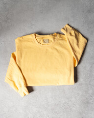 Blank Yellow Crewneck Sweatshirt Folded on Concrete Background, Stylized Sleeves, Natural Lighting with Bold Shadows, Simple Product Shot with Blank Tag, Casual Apparel Photography Mockup Template