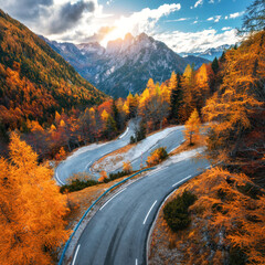 Aerial view of curvy mountain road and orange forest in golden autumn in Slovenia. Top view of winding road, colorful red trees, sky, rocks  in fall. Empty road in woods. Landscape with roadway