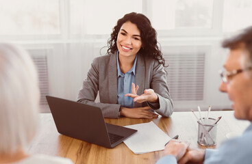 Offering Tours. Smiling mexican travel agent working with happy mature clients in office, gesturing, using laptop