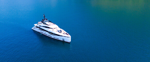 A snow-white modern yacht stands at anchor in an azure bay