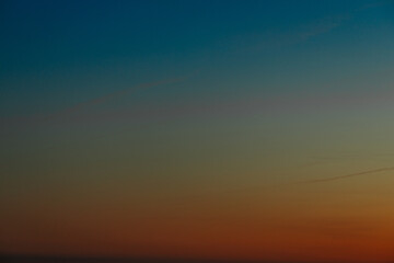 A vibrant sunset showcasing a gradient of colors from deep blue to orange and red near the horizon. The clear sky creates a tranquil atmosphere with a subtle transition of hues