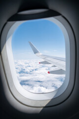 View of airplane wing through window with clouds and blue sky