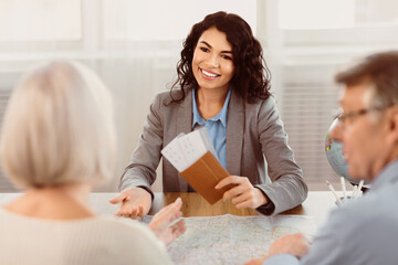 Mature couple sitting with manager at the travel agency office prepairing for a summer vacation, agent holding tickets