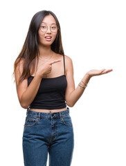 Young asian woman wearing glasses over isolated background amazed and smiling to the camera while presenting with hand and pointing with finger.