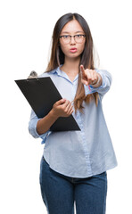 Fototapeta premium Young asian business woman holding clipboard over isolated background pointing with finger to the camera and to you, hand sign, positive and confident gesture from the front