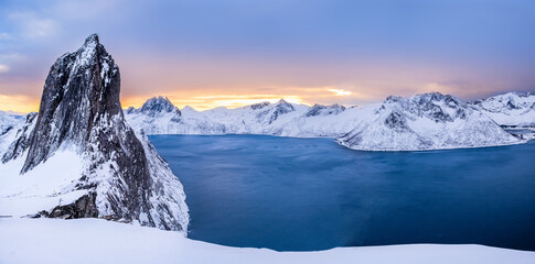 Panorama of Segla mountain peak and Fjord seen from Hesten trail near Fjordgard on Senja island, Norway in winter. Scenic winter landscape with snowy mountains range and cold fjord water at sunset