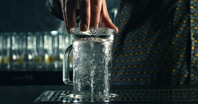 Super slow motion close up of barman or bartender washing transparent beer mug with automatic glass rinser with water spray and splashing drops in bar at 1000 fps.
