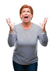 Atrractive senior caucasian redhead woman over isolated background crazy and mad shouting and yelling with aggressive expression and arms raised. Frustration concept.