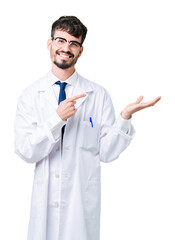 Young professional scientist man wearing white coat over isolated background amazed and smiling to the camera while presenting with hand and pointing with finger.