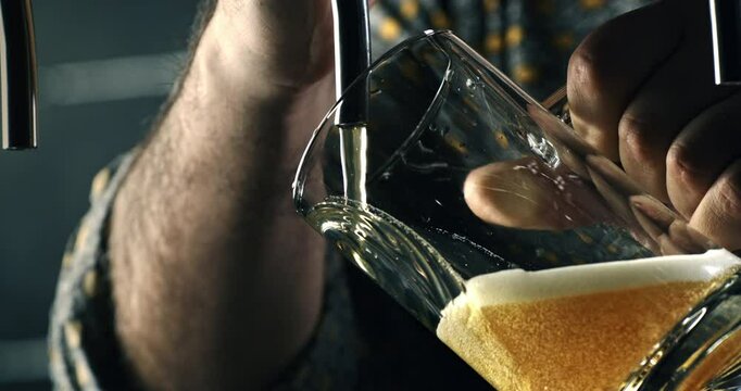 Super slow motion macro of frothy golden icy fresh cold beer is being poured in transparent glass by barman or bartender from beer tap while serving to customer at bar pub at 1000 fps.