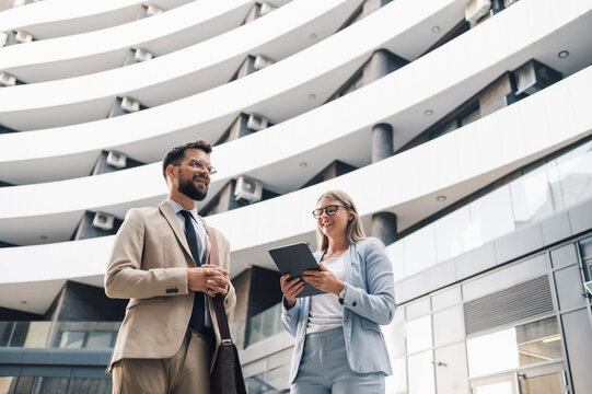 Business partners discussing project using tablet in front of modern office building