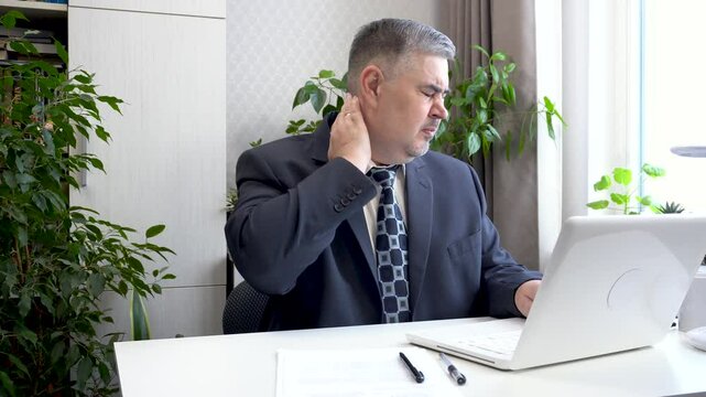 A man working at a computer has a sore neck. He rubs his neck to relieve the pain. Suitable for content about freelancing and remote work.