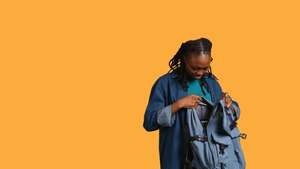 Happy woman taking laptop out of backpack, preparing to start job shift, isolated over studio background. Smiling african american employee unpacking notebook, going to work, camera B