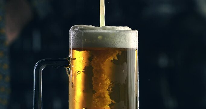 Super slow motion close up of frothy golden icy fresh cold beer is being poured in transparent glass by barman or bartender while serving to customer at bar pub at 1000 fps.