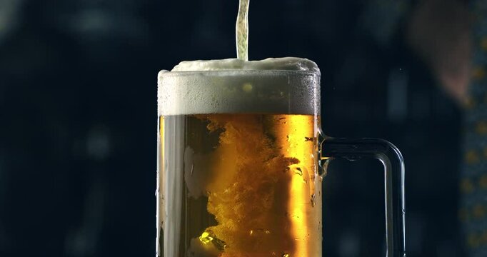 Super slow motion close up of frothy golden icy fresh cold beer is being poured in transparent glass by barman or bartender while serving to customer at bar pub at 1000 fps.