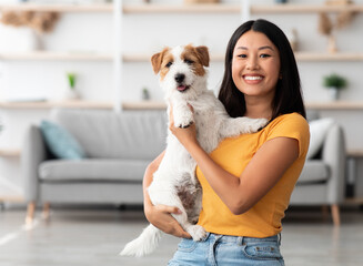 Portrait of cheerful young asian woman in casual outfit carrying her sweet fluffy dog jack russel...