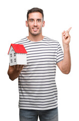 Handsome real estate agent holding a house very happy pointing with hand and finger to the side