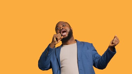 Upbeat african american singer holding microphone, performing tunes, isolated over yellow studio background. Energetic musician singing to imaginary crowd, doing karaoke, camera A