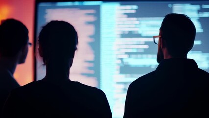 Three software developers work intensely on code in a dim office, showcasing their expertise in programming and web development