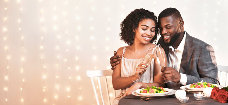 Romantic african american couple drinking champagne in fancy restaurant, having dinner with candles