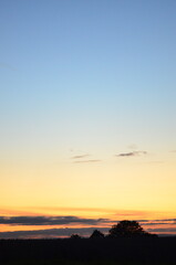 A scenic background of trees on the horizon with the setting sun casting a warm glow. Dramatic clouds stretch across the colorful autumn sky, creating a breathtaking and atmospheric sunset view