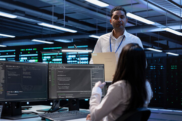 Team of engineers in data center looking for firewall misconfigurations affecting servers. Multiracial workers in server room check systems bottlenecks leading to sluggish data transfer rates