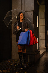 vertical Young fashionable latina girl sheltering from the rain with a transparent umbrella at night