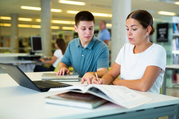 Obraz premium View on young european students studying together with a laptop in library