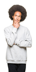 Young african american man with afro hair wearing sporty sweatshirt with hand on chin thinking about question, pensive expression. Smiling with thoughtful face. Doubt concept.