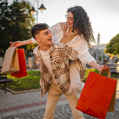 young woman is riding her man with bags while going shopping together